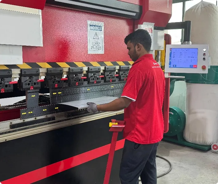 A factory worker operating a red industrial press brake machine, bending a metal sheet.