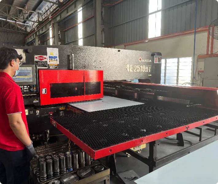 Technician operating an AMADA AE 2510 NT turret punch press on a metal sheet in a factory
